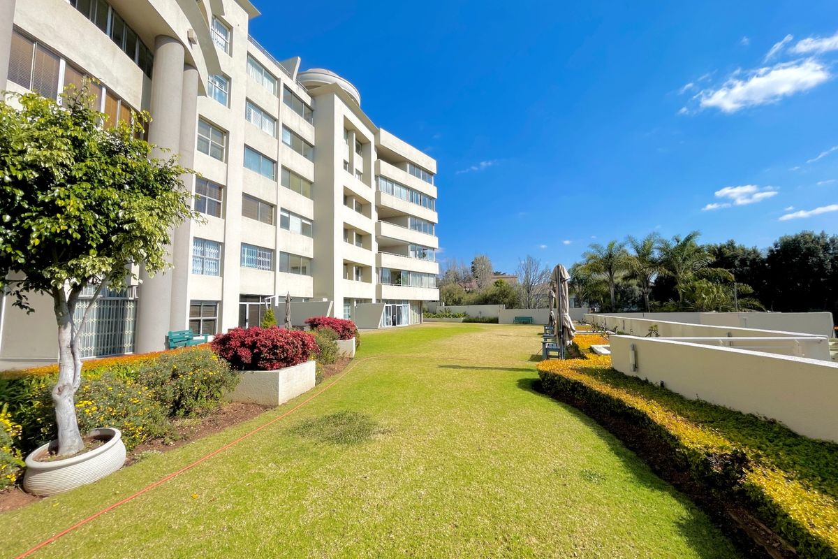 A well-maintained communal garden area featuring manicured lawns and landscaped borders, situated at the rear of a multi-story apartment complex.