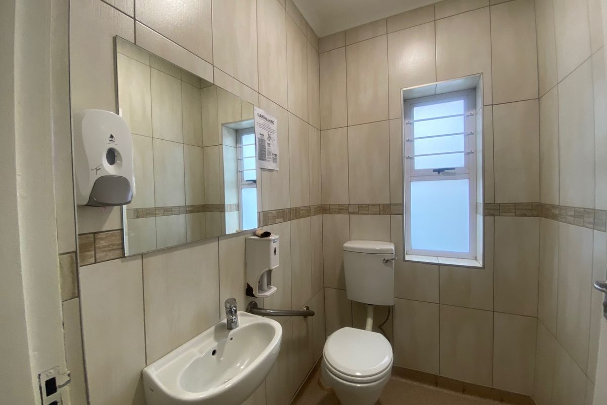 A clean, functional commercial restroom featuring full-height ceramic wall tiling, a wall-mounted basin, toilet, and safety grab rail.