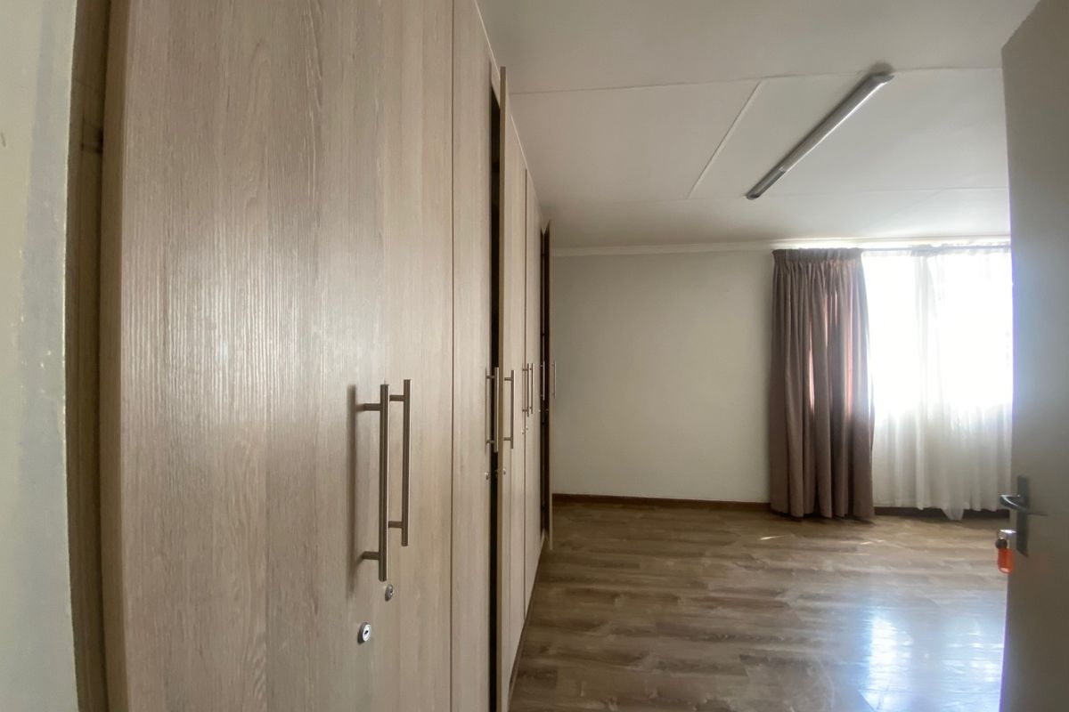 Spacious bedroom featuring light wood-finish built-in cupboards, durable laminate flooring, and ample natural light from the window.