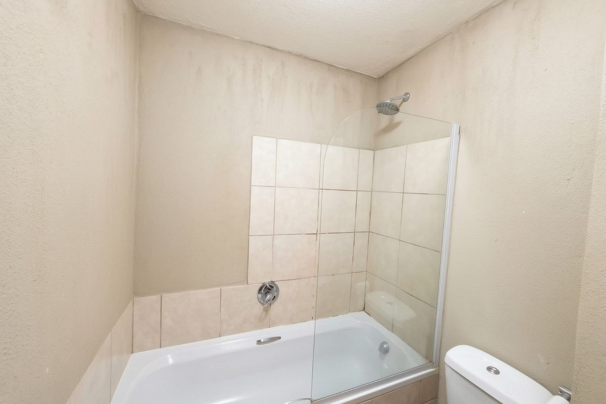 A compact bathroom featuring a bathtub with a glass shower screen, tiled splashback, and a standard toilet.