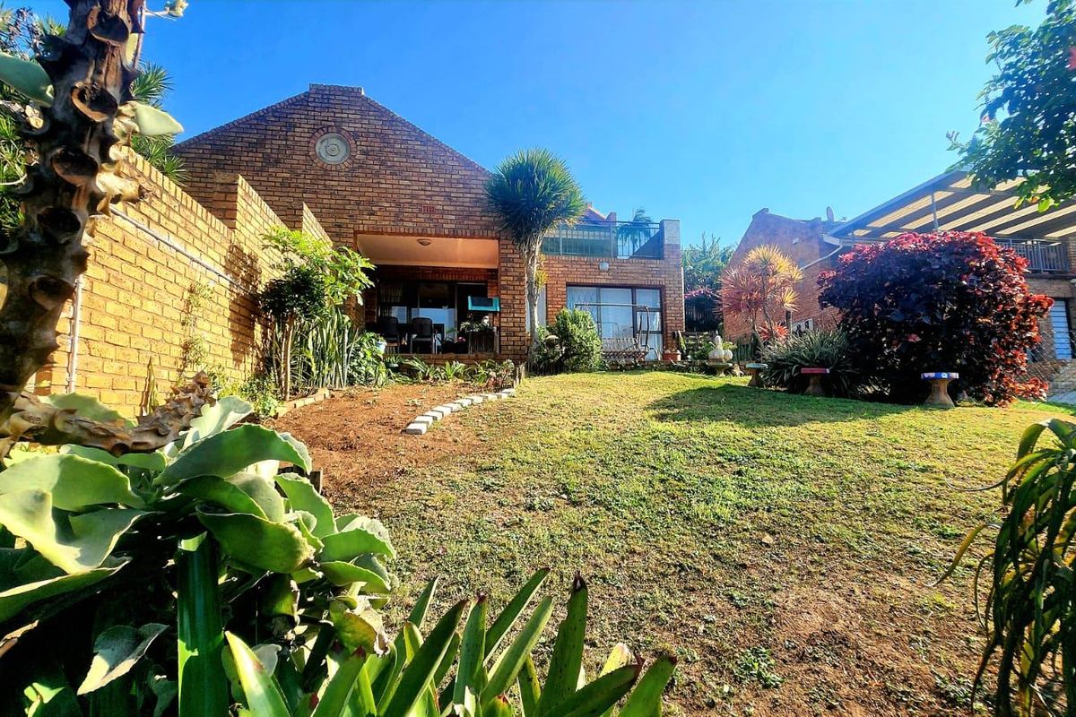 Rear view of the townhouse featuring a face brick facade, a covered patio area, and a well-established garden with lawn.