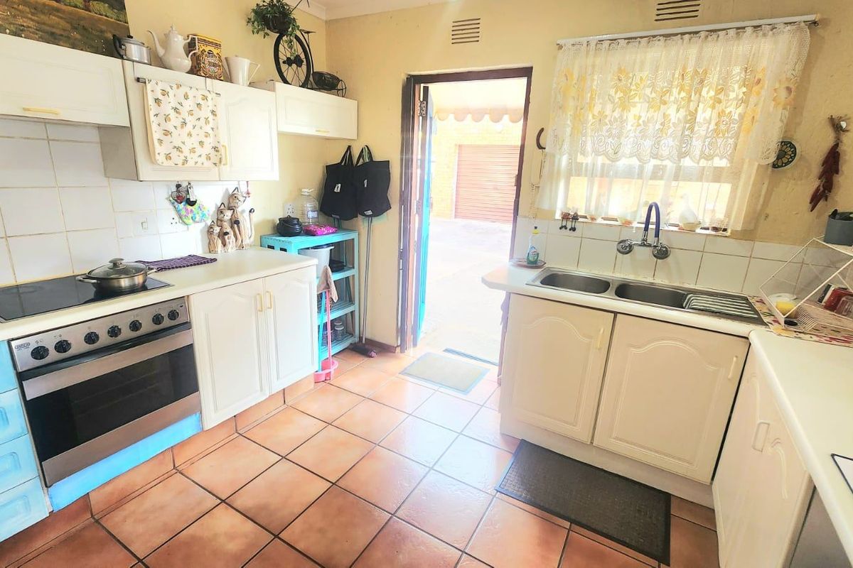 A functional kitchen featuring built-in cabinetry, a double basin sink, and an electric stove with oven, finished with tiled flooring and splashbacks.