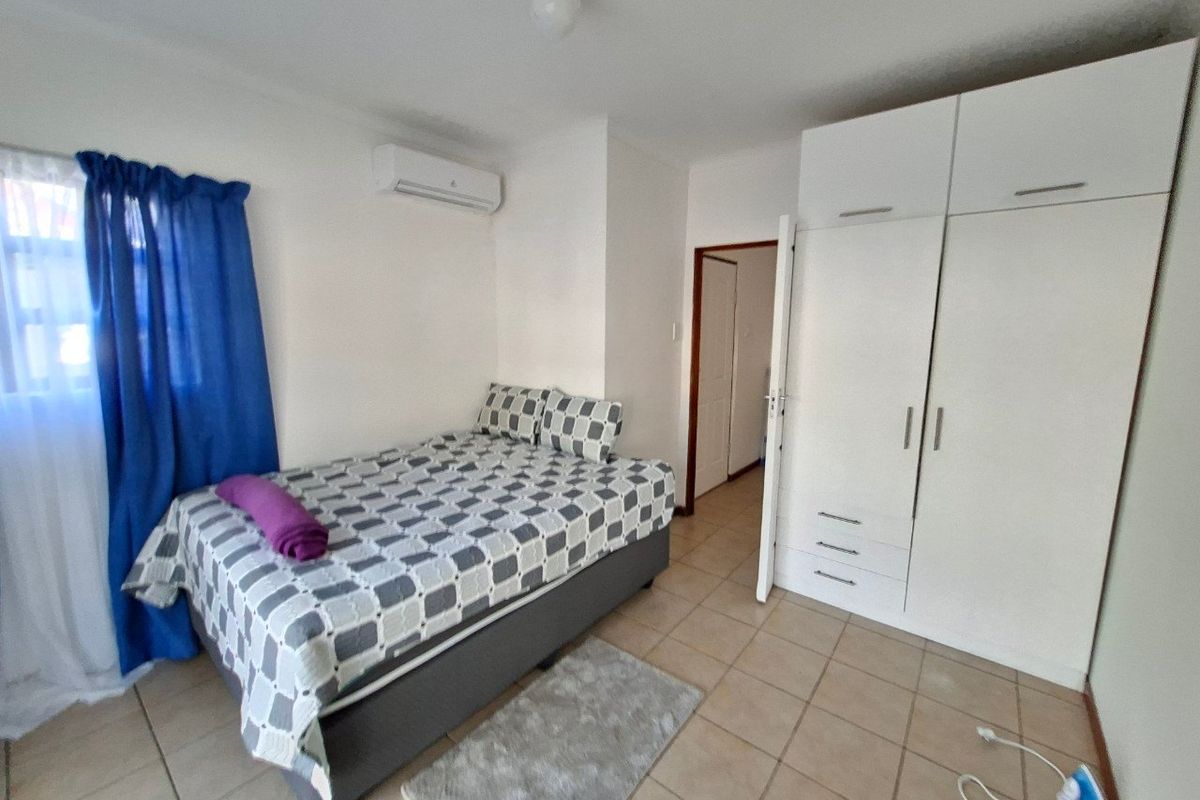 A functional bedroom featuring tiled flooring, a built-in wardrobe, and a wall-mounted split-system air conditioning unit.