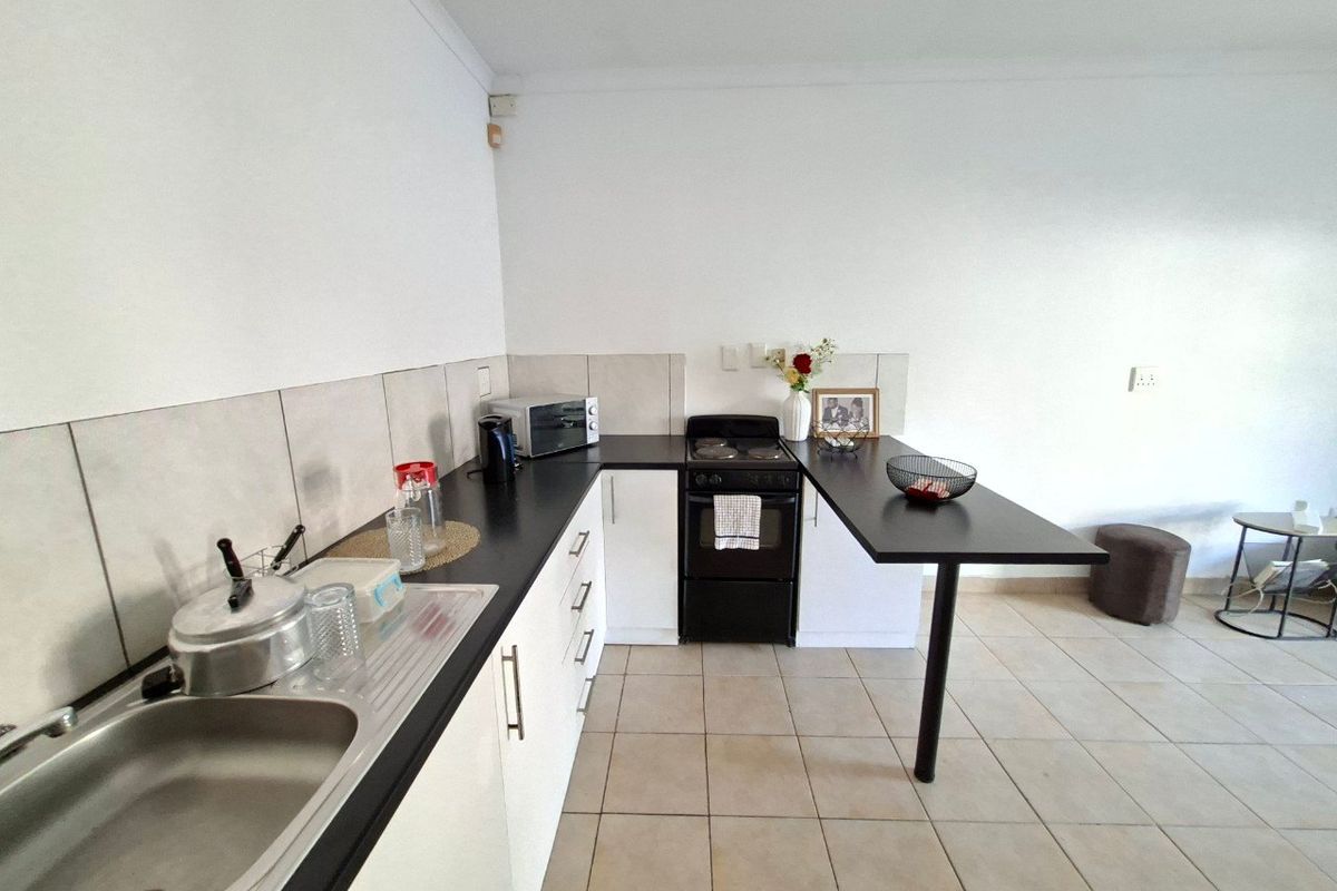 A functional kitchen featuring white cabinetry, black countertops, a built-in oven with hob, and a convenient breakfast bar extension.