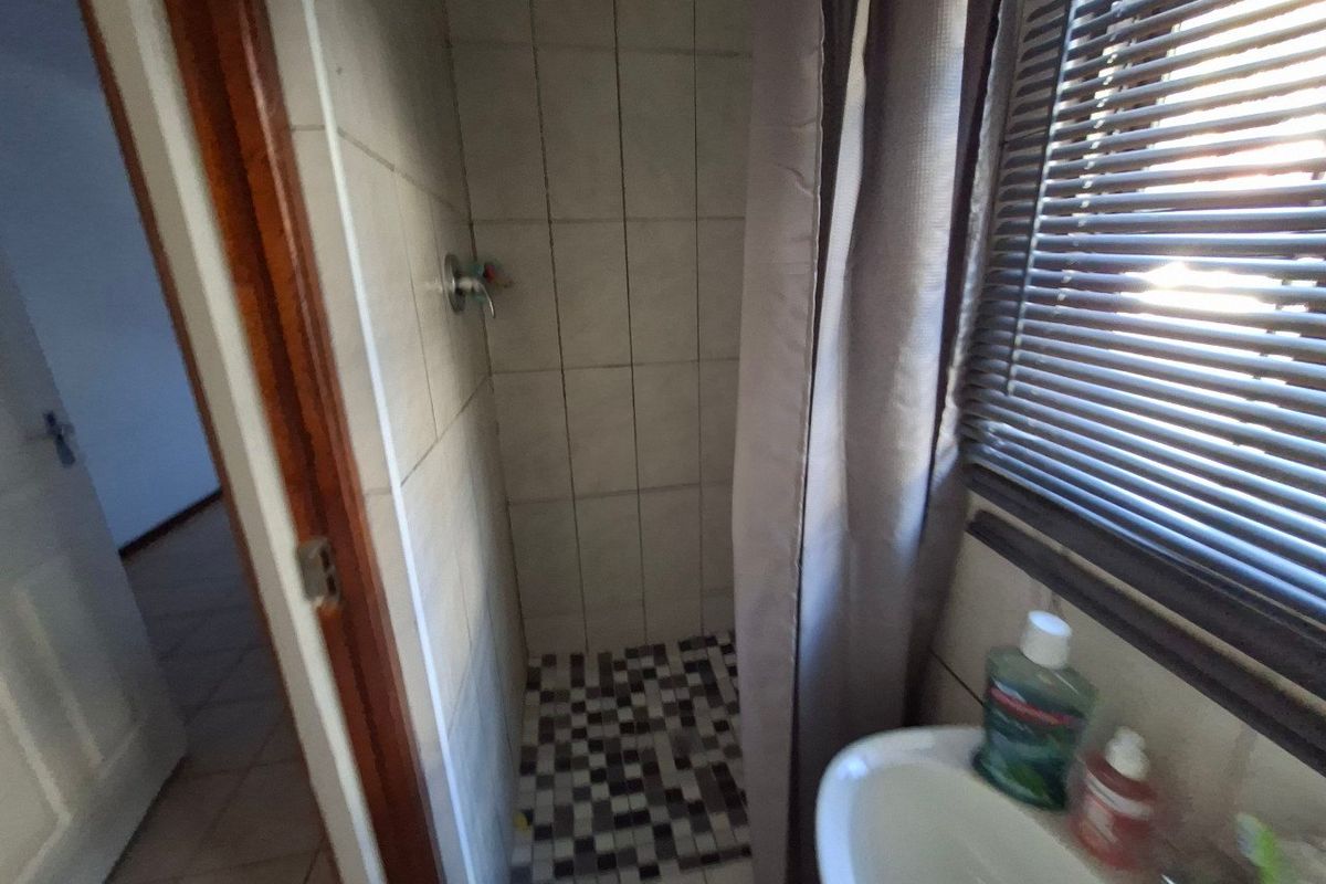 A functional bathroom featuring a shower with tiled walls and mosaic flooring, complemented by a washbasin and window blinds.