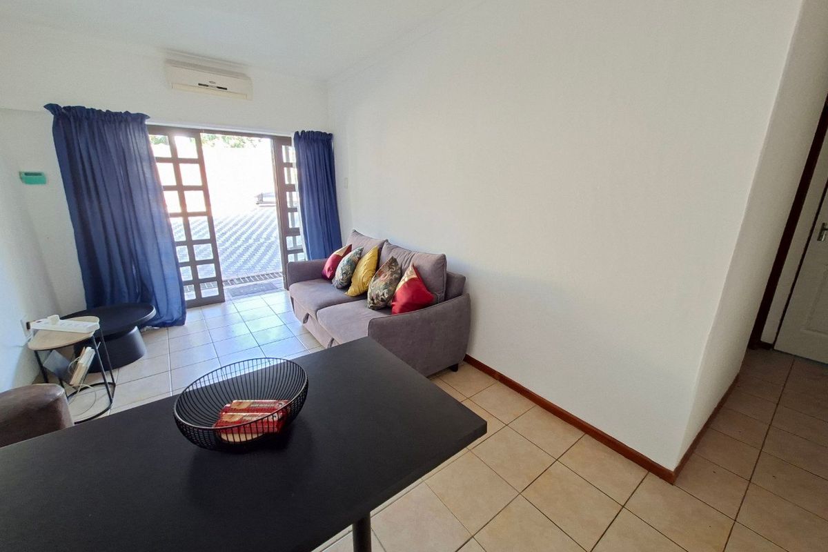 A living room featuring tiled flooring, a wall-mounted air conditioning unit, and a glass sliding door providing access to the exterior.