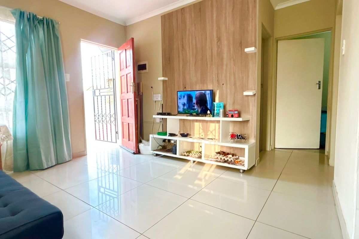A bright living room featuring large format floor tiles, a modern wood-look feature wall, and direct access to the exterior via a security gate.