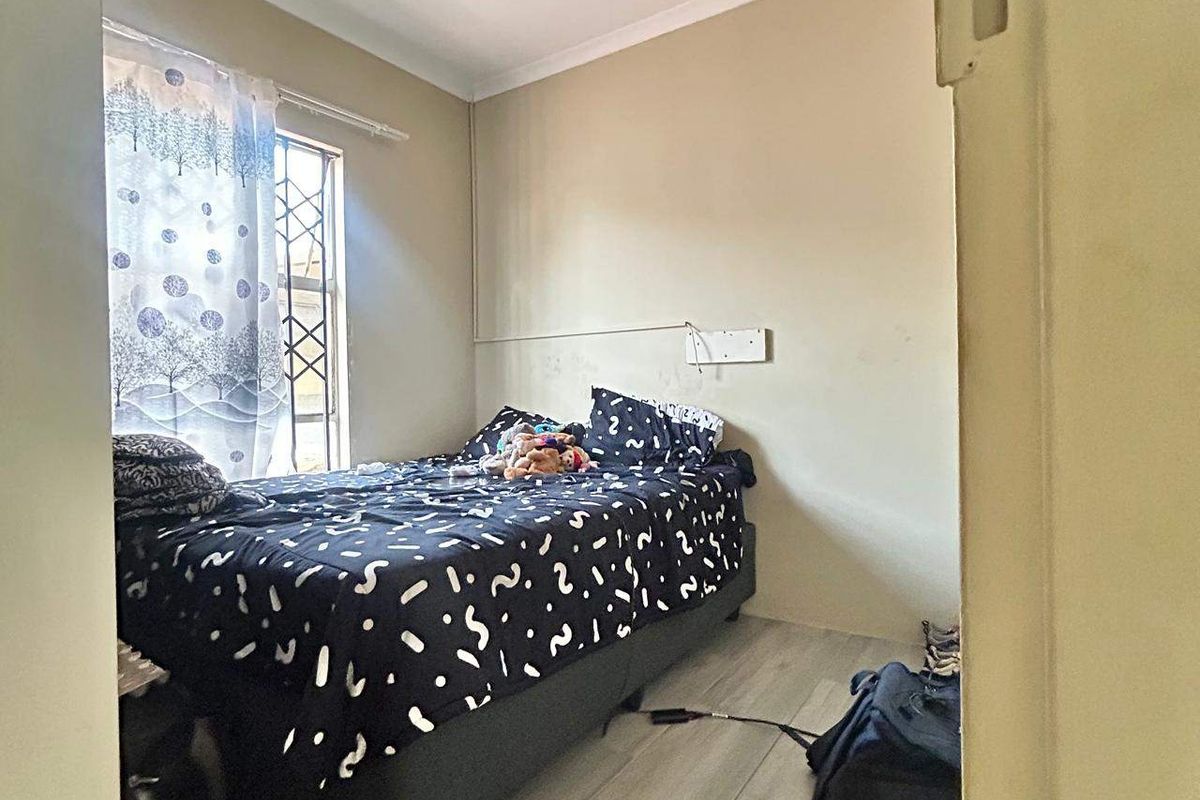 A compact bedroom featuring tiled flooring and a security gate on the window, with a visible water stain on the ceiling.