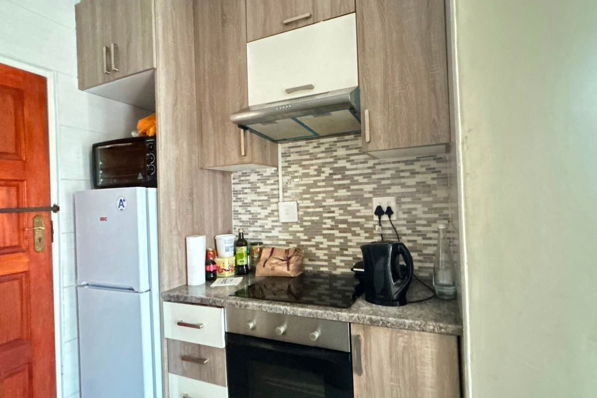 Compact kitchen featuring wood-look cabinetry, mosaic tile backsplash, integrated oven, hob, and extractor fan, providing a functional cooking space.