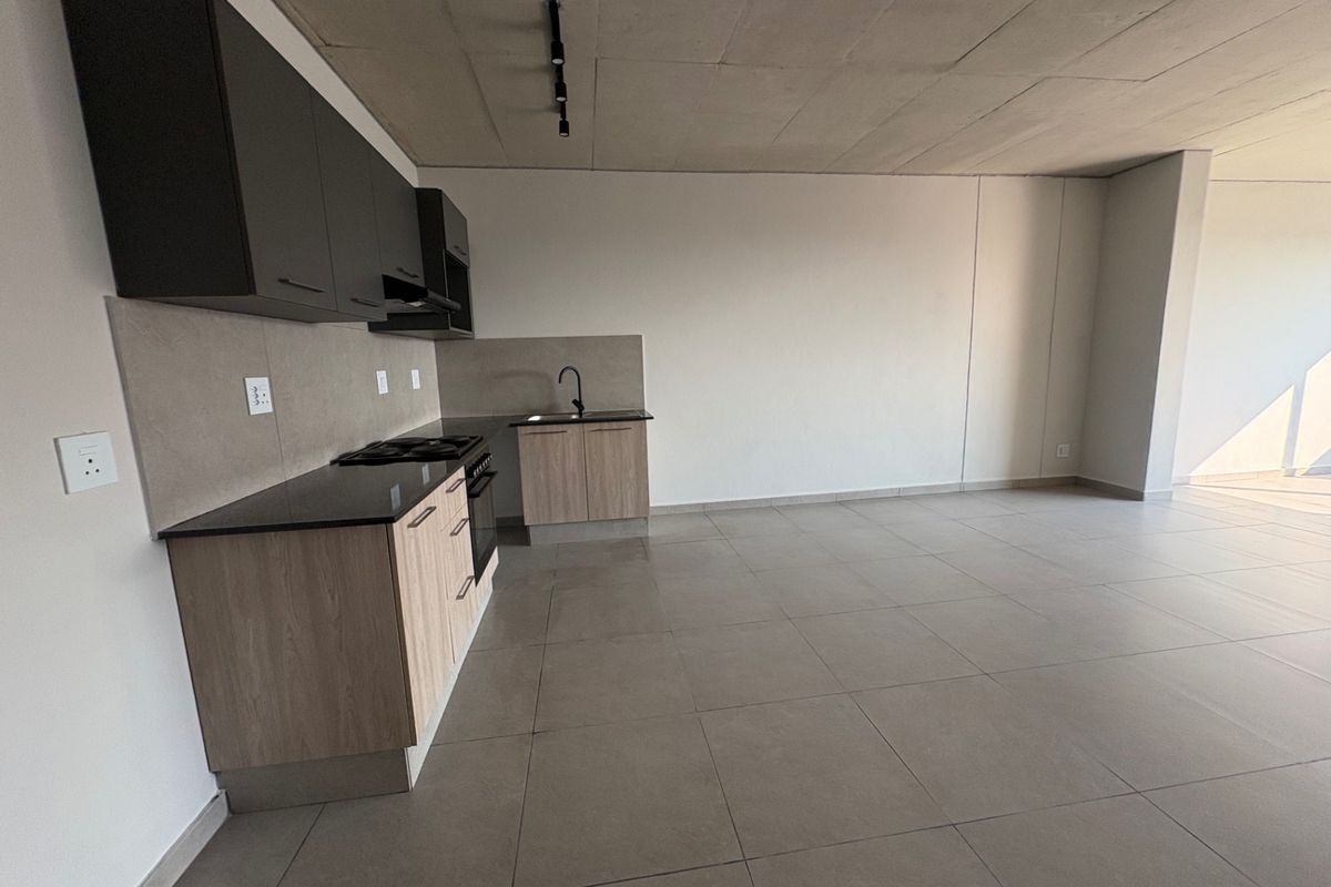 Modern open-plan kitchen featuring sleek cabinetry, granite countertops, built-in appliances, and tiled flooring, set within a spacious, minimalist living area with exposed concrete ceilings.