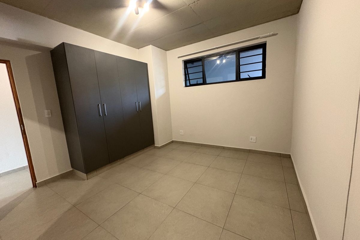 A clean, modern bedroom featuring tiled flooring, an exposed concrete ceiling, and a built-in wardrobe with dark cabinetry.
