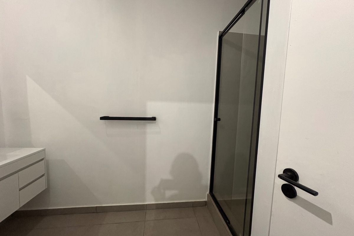 A modern, minimalist bathroom featuring a wall-mounted vanity, a sleek shower enclosure with a black frame, and neutral floor tiling.