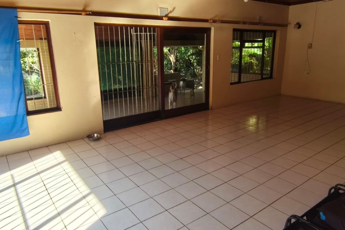 Spacious, light-filled living area featuring neutral tiled flooring and large sliding glass doors providing direct access to the garden.