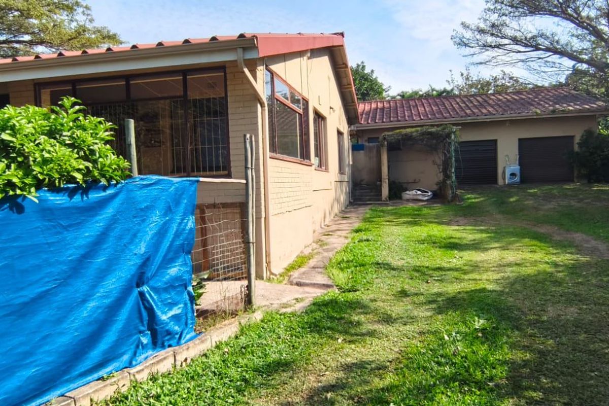 Rear view of the property featuring a brick exterior, tiled roof, and a detached double garage set within a large garden area.