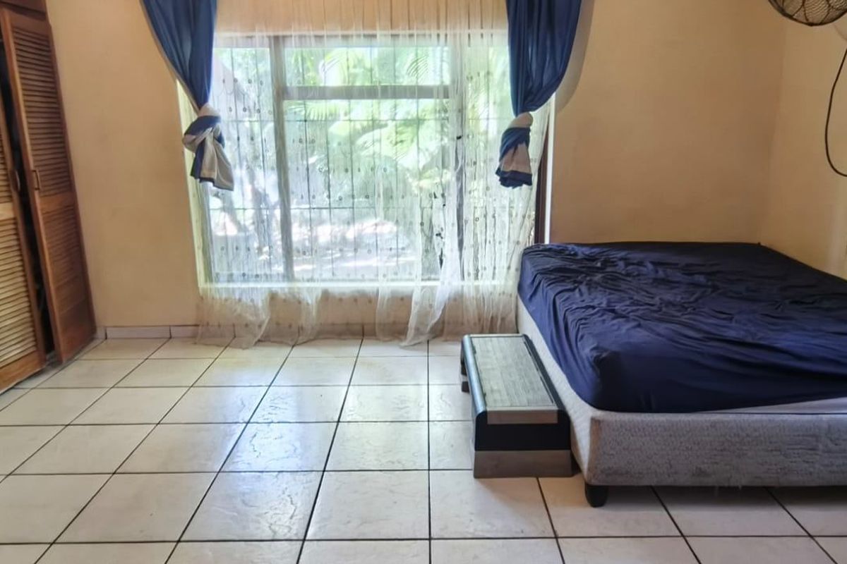 A bedroom featuring tiled flooring, a large window with security bars, and a built-in wooden wardrobe.