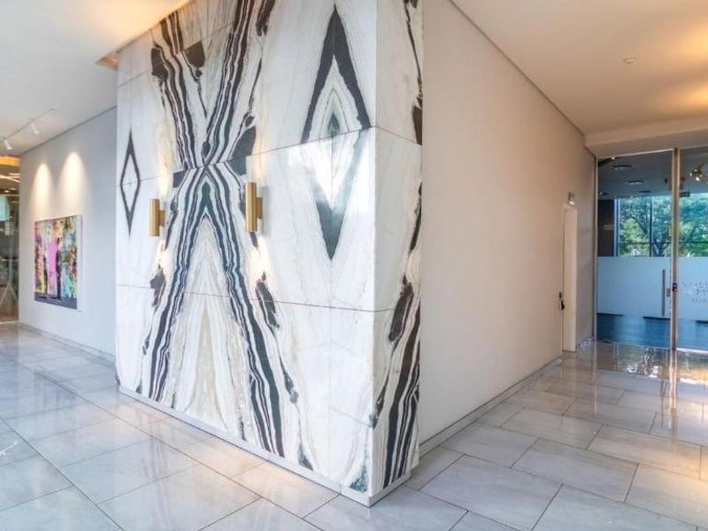Modern apartment building lobby featuring polished marble wall cladding, sleek tiled flooring, and contemporary wall-mounted lighting fixtures.