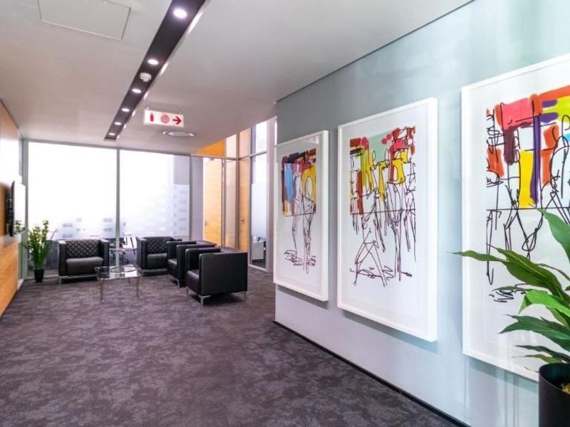 A modern, well-lit hallway or reception area featuring glass partitions, recessed ceiling lighting, and high-quality carpeting.