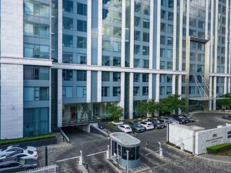 Modern high-rise apartment building exterior featuring a secure gated entrance, paved driveway, and contemporary glass and stone facade.
