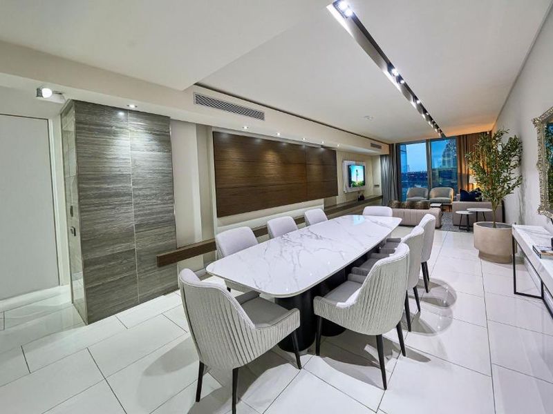 A modern open-plan living and dining area featuring sleek tiled flooring, recessed ceiling lighting, and high-end wall paneling finishes.