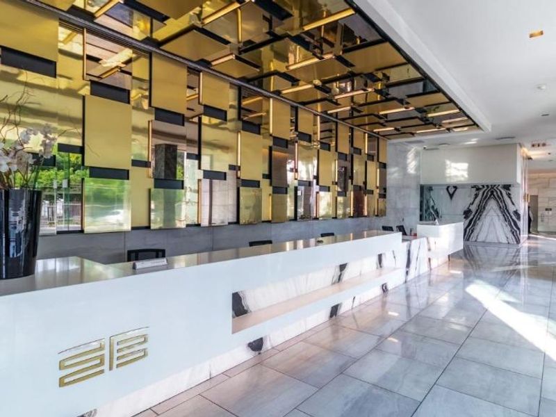 Modern apartment building lobby featuring a sleek reception desk, polished marble flooring, and a decorative gold-paneled ceiling feature.