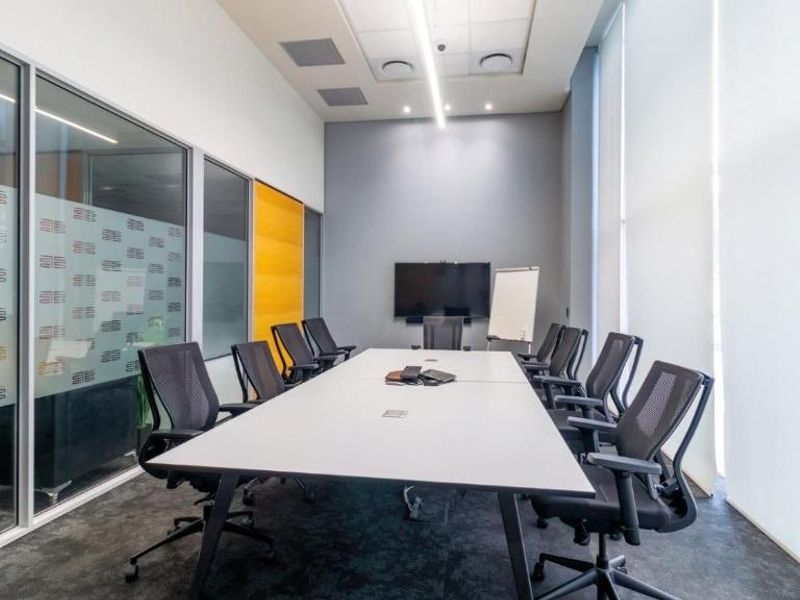 A modern, professional meeting room featuring glass partitions, recessed lighting, and large windows with roller blinds, suitable for corporate use.
