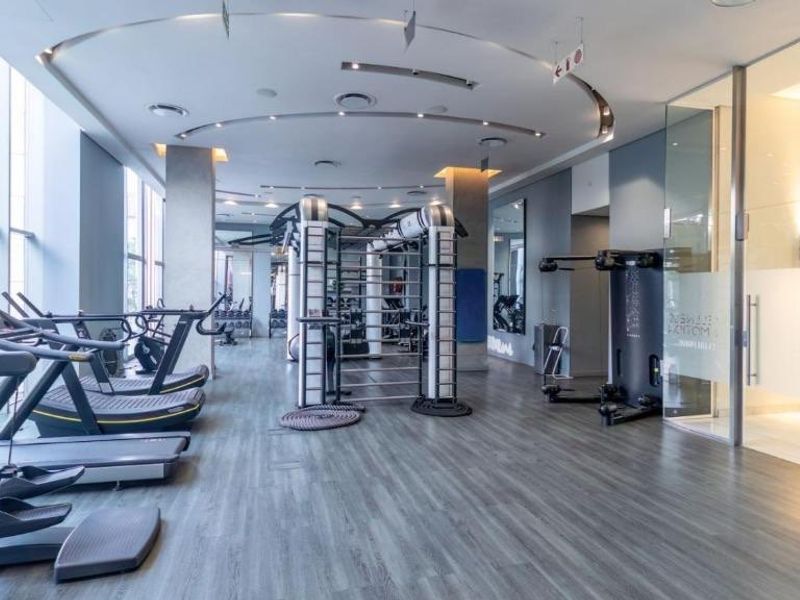 A modern, well-equipped fitness facility featuring floor-to-ceiling windows, recessed ceiling lighting, and durable wood-look flooring.
