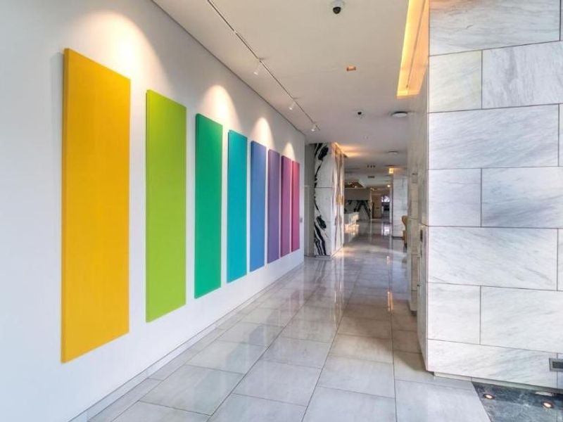 A modern, well-lit hallway featuring polished marble flooring, recessed ceiling lighting, and decorative wall panels in a vibrant color palette.