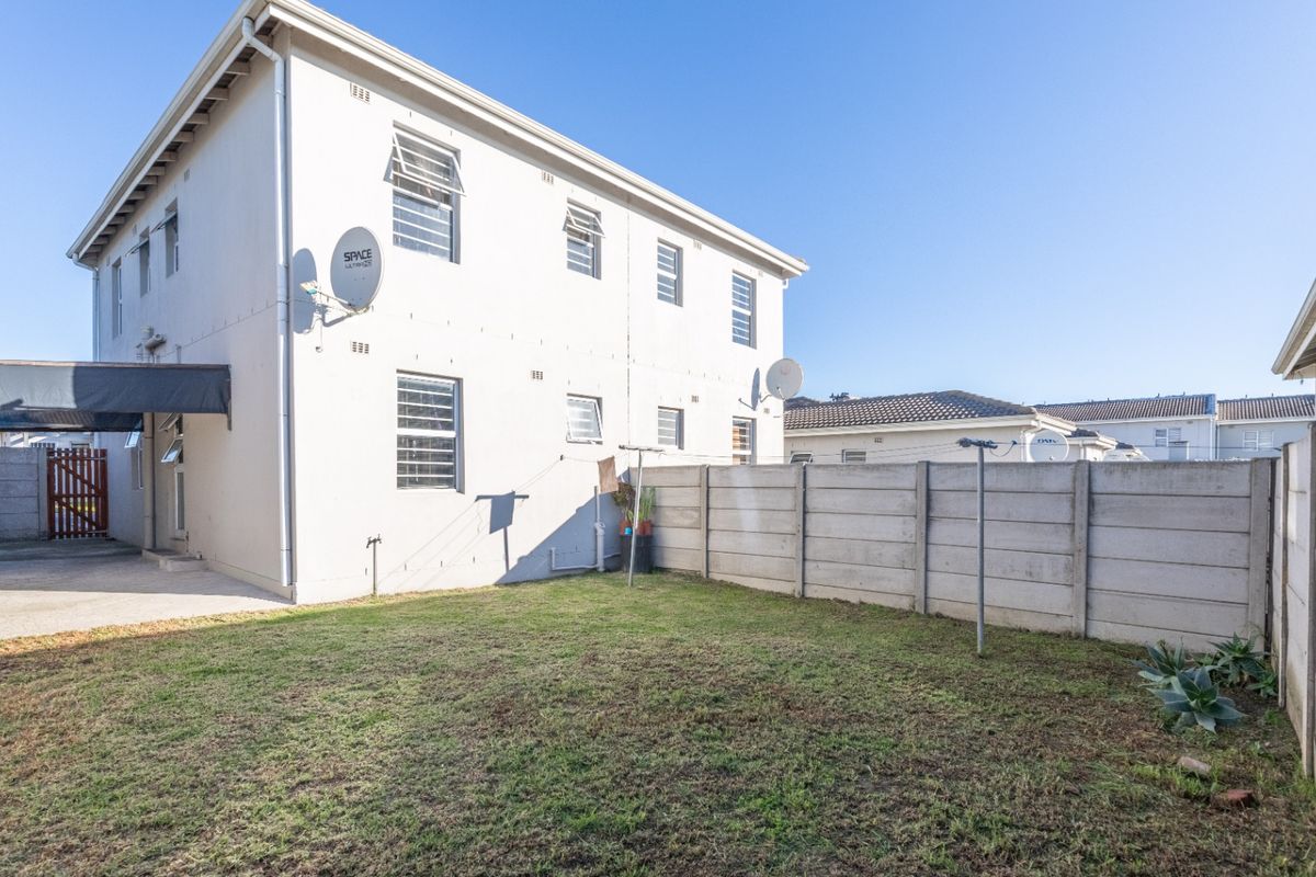 Rear view of the property featuring a private garden, precast concrete boundary walls, and a paved driveway area.