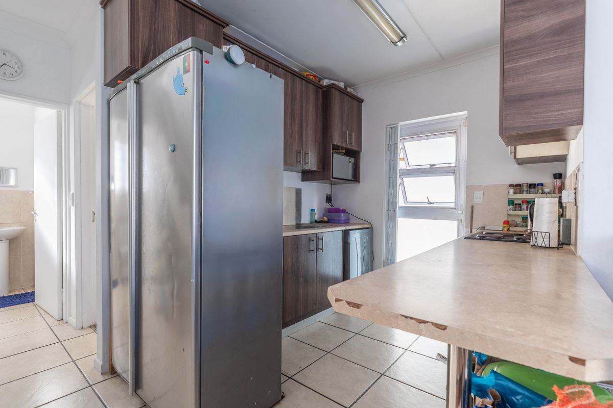 Functional kitchen featuring dark laminate cabinetry, tiled flooring, and a breakfast bar, with an adjacent small bathroom area visible.