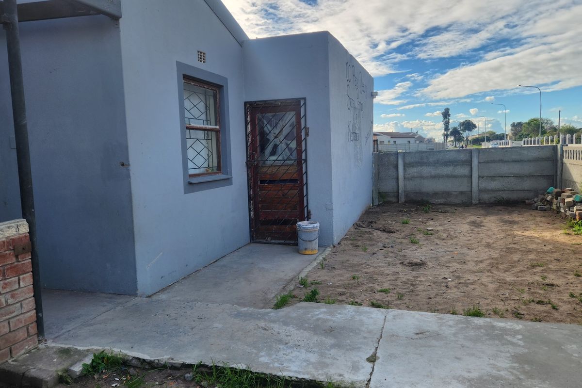 Rear exterior view of the property featuring a concrete walkway, security gate, and precast boundary wall with visible graffiti on the exterior wall.