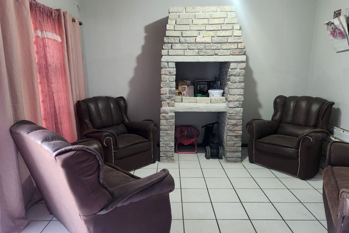 A living room featuring a central brick fireplace and tiled flooring, offering a functional space with potential for cosmetic updates.