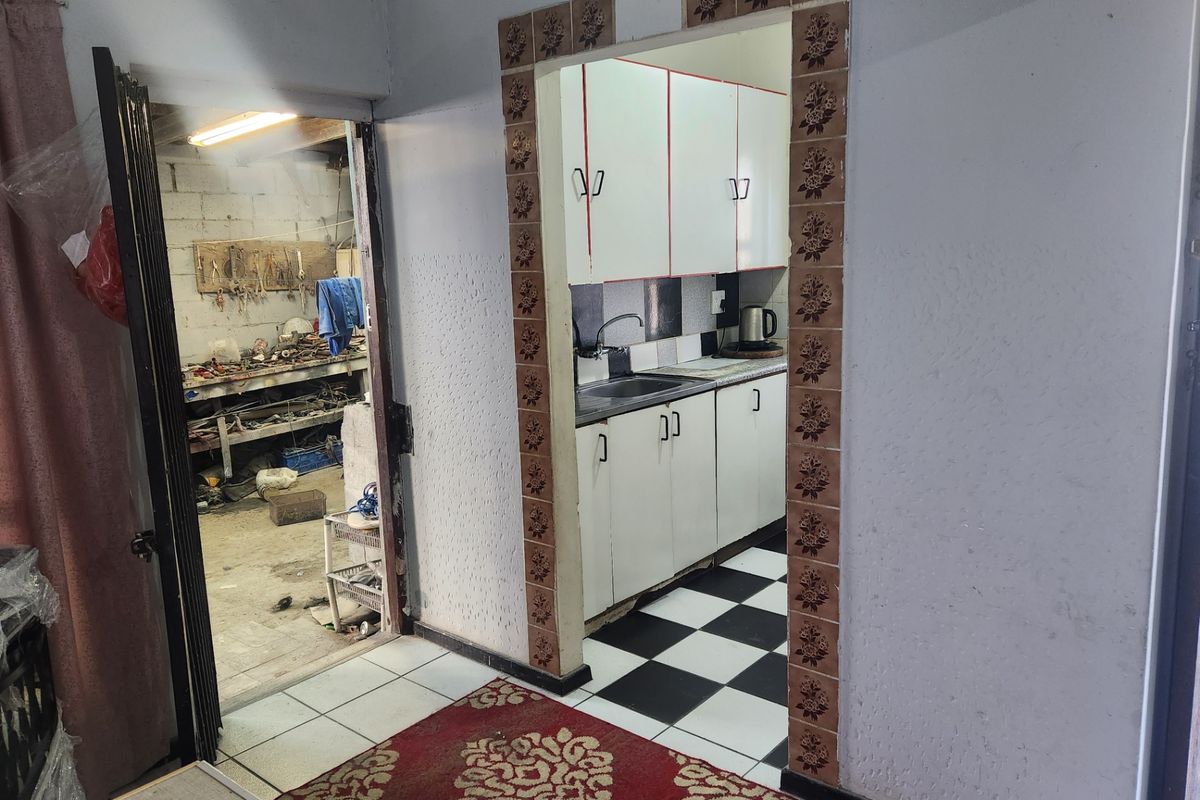 A dated kitchen featuring white cabinetry, a stainless steel sink, and a distinctive checkerboard floor, viewed through a decorative tiled doorway.