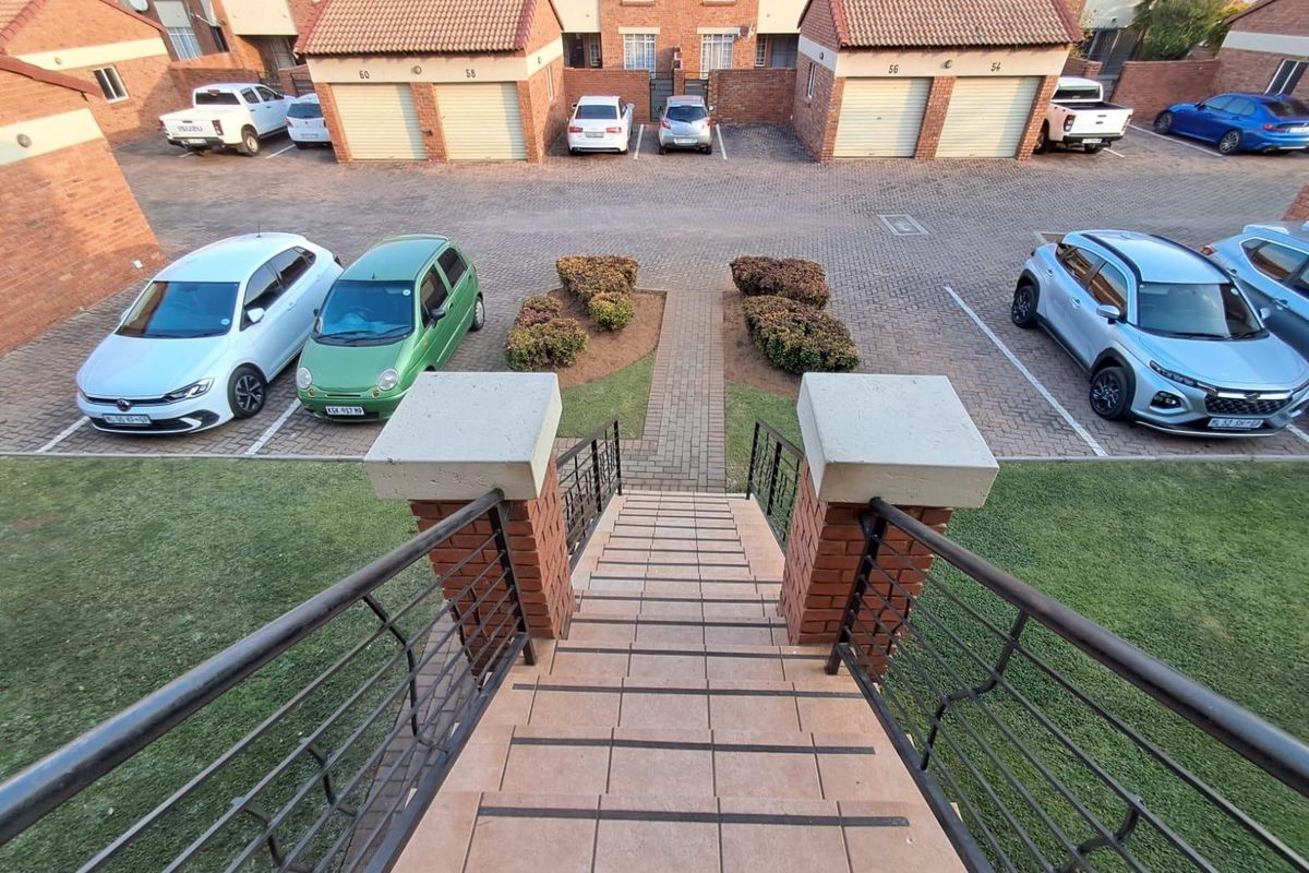 Elevated view overlooking a residential complex courtyard featuring a tiled staircase, brick paved parking area, and multiple garage units.