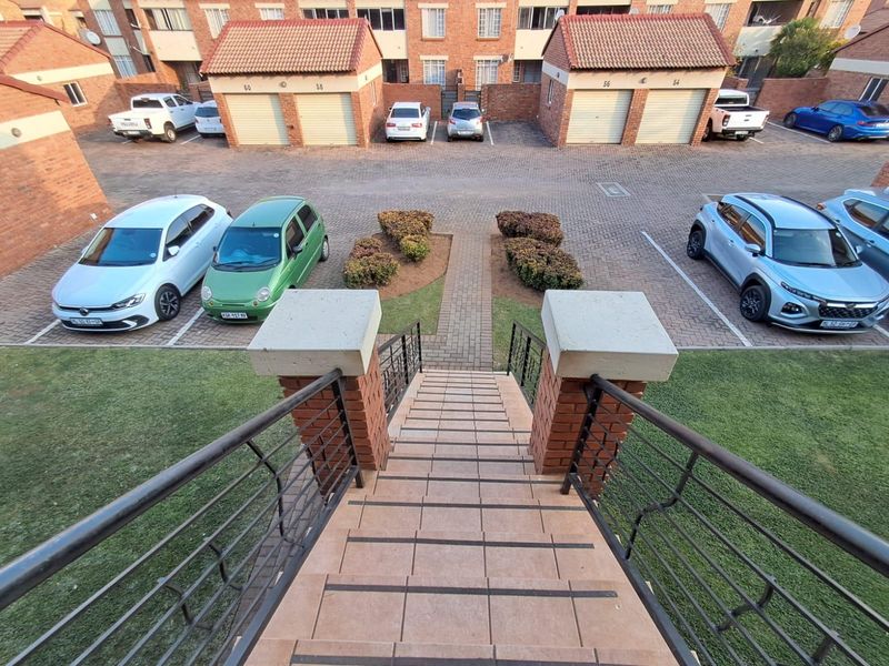 Elevated view overlooking a residential complex courtyard featuring a tiled staircase, brick paved parking area, and multiple garage units.