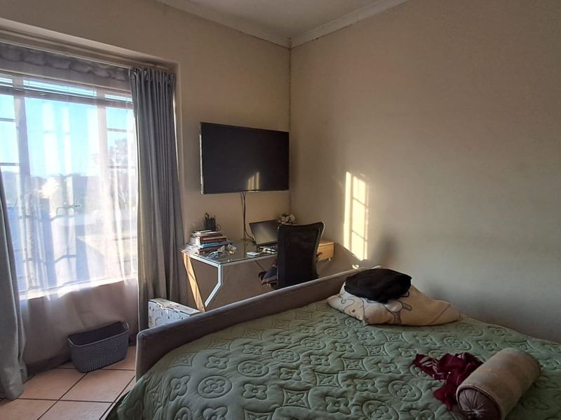 A functional bedroom featuring tiled flooring and a large window that provides natural light, with a wall-mounted television setup.