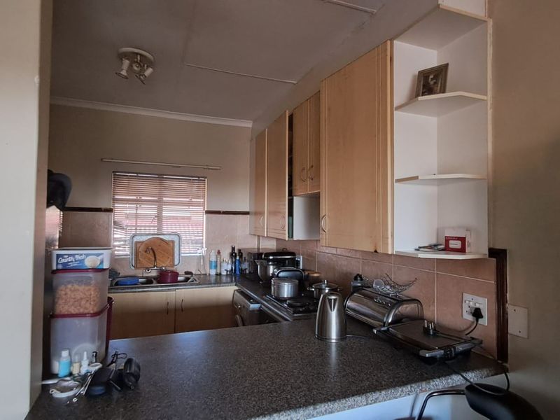 A compact kitchen featuring laminate cabinetry, granite countertops, a tiled backsplash, and a built-in hob, offering a functional layout with potential for modernization.