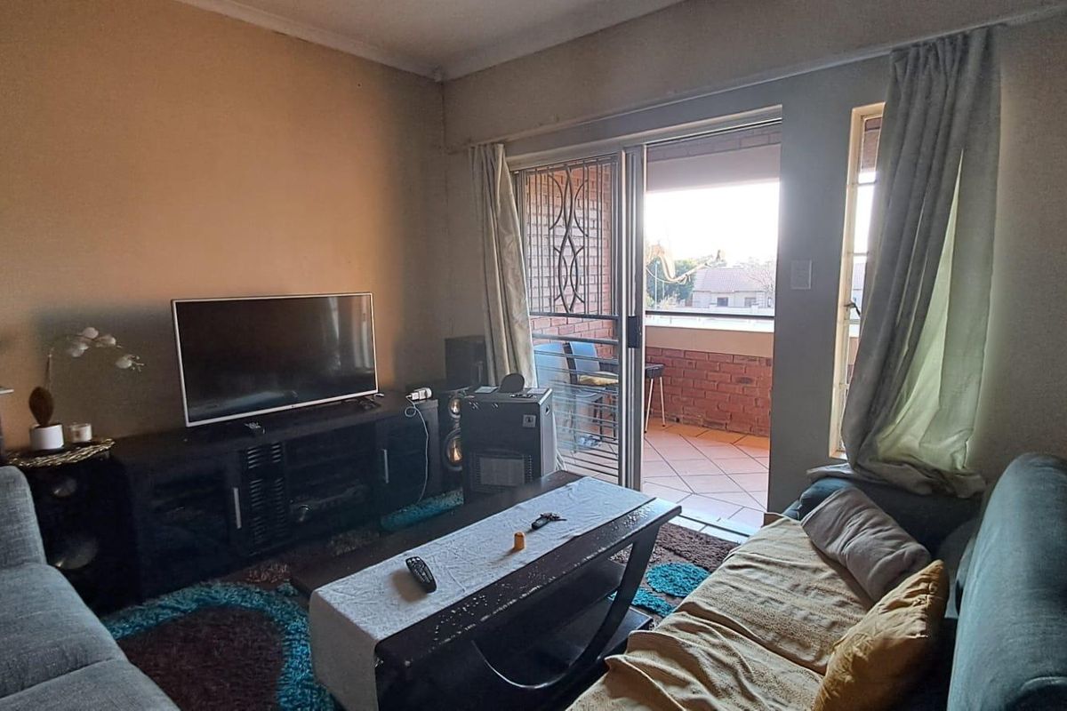 A living room featuring a sliding glass door with a security gate leading out to a tiled balcony.