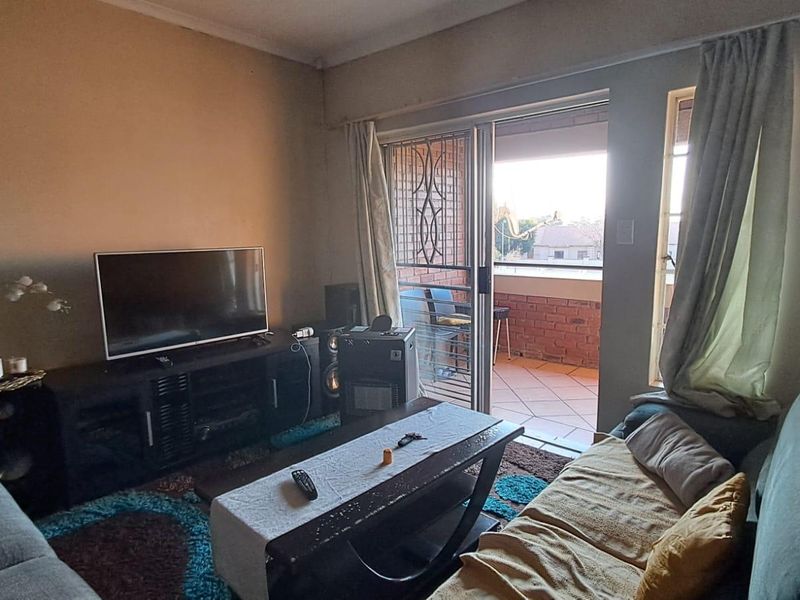 A living room featuring a sliding glass door with a security gate leading out to a tiled balcony.