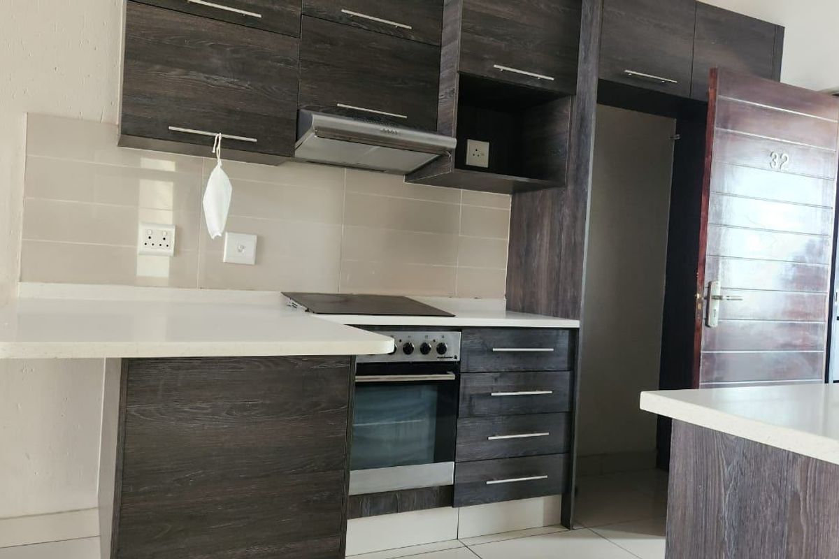 Modern kitchen featuring dark wood-grain cabinetry, stone countertops, built-in oven, hob, and extractor fan, with a clean tiled backsplash and neutral flooring.