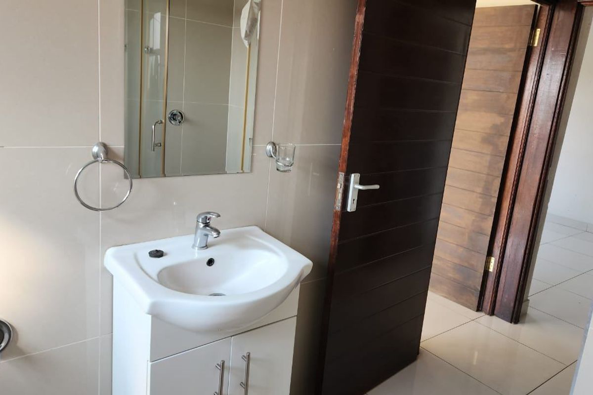A clean, modern bathroom featuring a white vanity basin with a mixer tap, wall-mounted mirror, and neutral wall tiling.