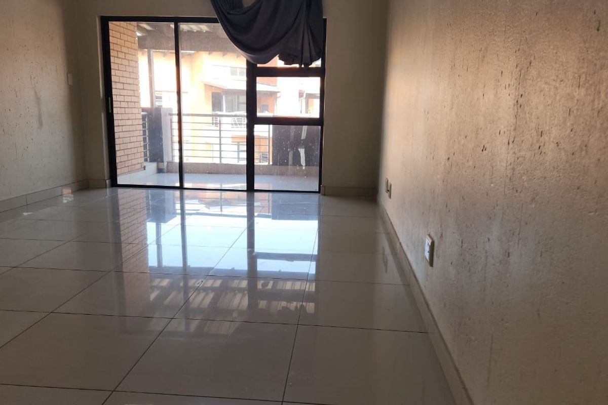 An empty living room featuring polished tiled flooring and a large sliding glass door providing access to an outdoor balcony area.