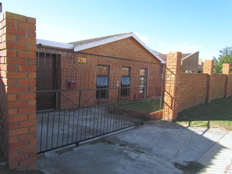 Front view of a face brick house featuring a secure metal gate, boundary wall, and a roller shutter garage door.