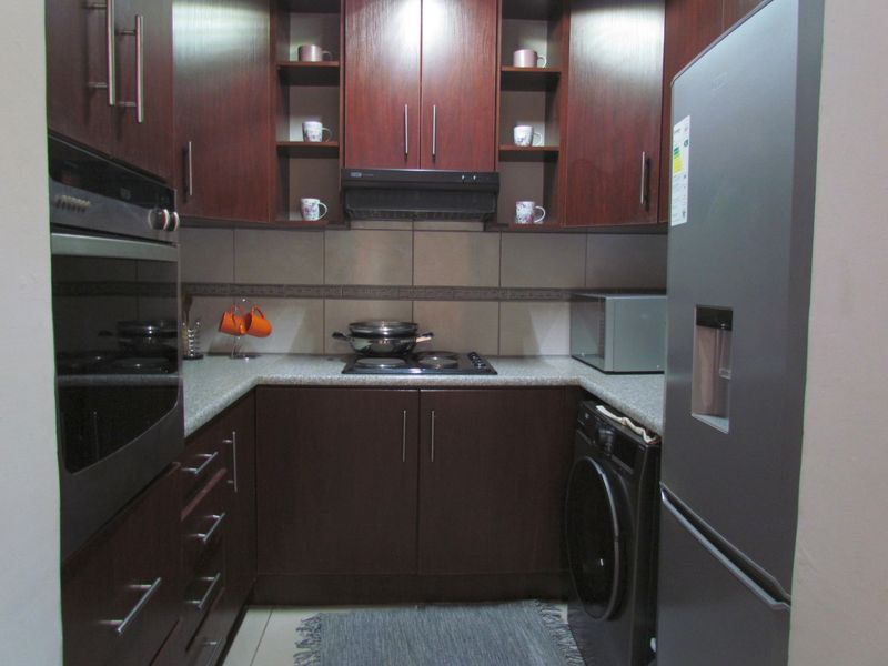 Compact kitchen featuring dark wood cabinetry, built-in oven, electric hob with extractor fan, and dedicated space for a washing machine.