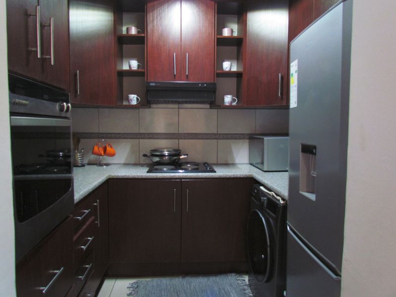 Compact kitchen featuring dark wood cabinetry, granite-look laminate countertops, built-in oven, hob, and extractor fan with a tiled backsplash.