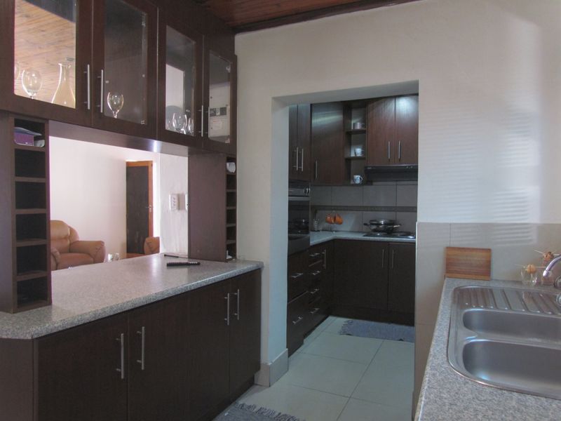 A functional kitchen featuring dark wood cabinetry, laminate countertops, built-in oven and hob, and tiled flooring with a separate scullery area.