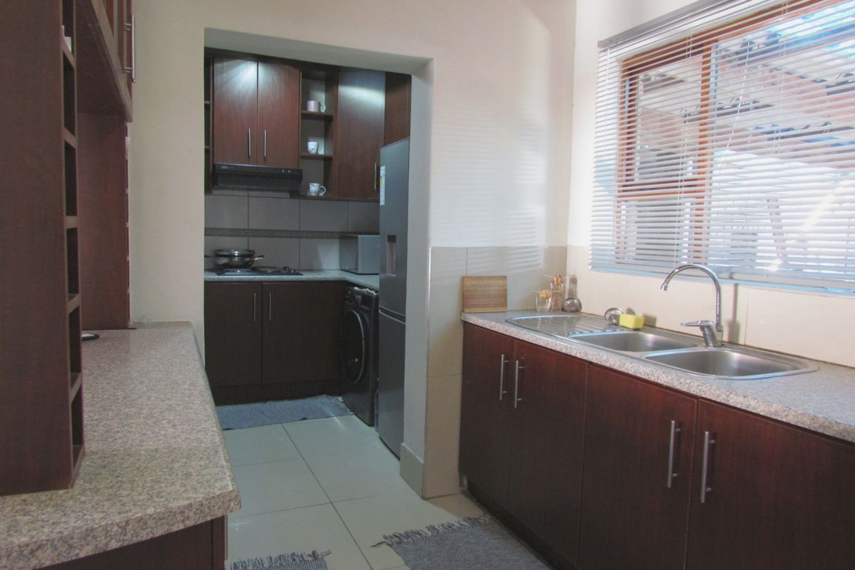 A functional kitchen featuring dark wood cabinetry, laminate countertops, a double stainless steel sink, and tiled flooring with an adjoining scullery area.