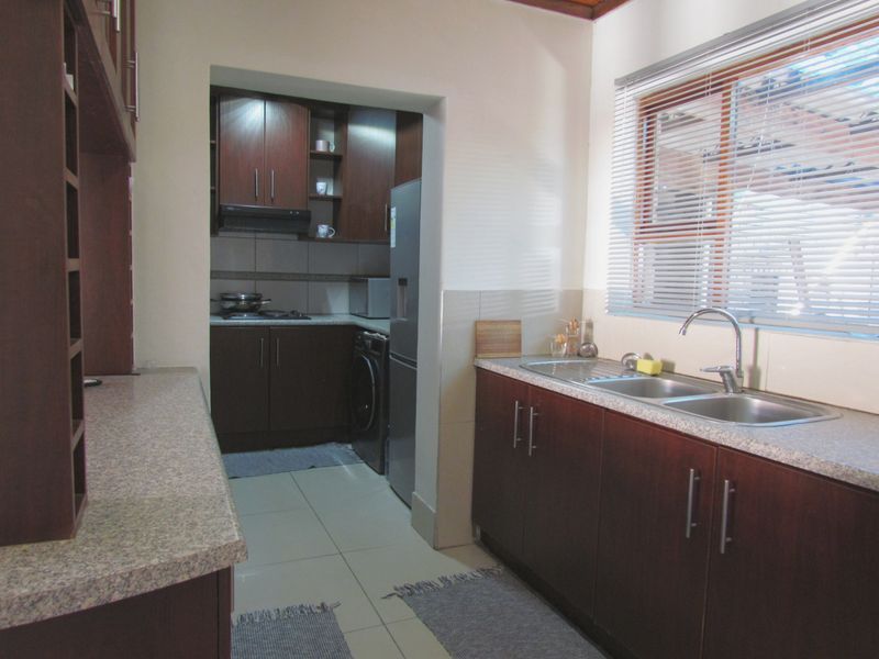 A functional kitchen featuring dark wood cabinetry, laminate countertops, a double stainless steel sink, and tiled flooring with an adjoining scullery area.