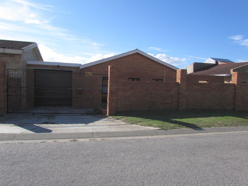 Front exterior view of a single-story face brick house featuring a tiled roof, enclosed perimeter wall, and a metal garage door.