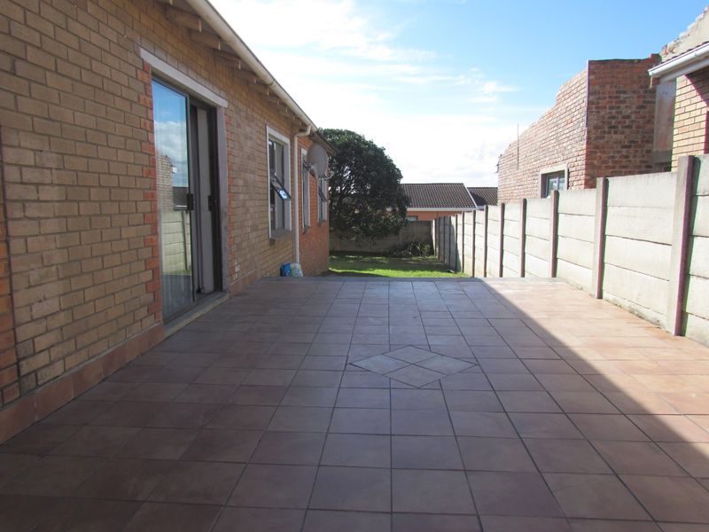 A spacious tiled patio area featuring facebrick exterior walls and a sliding glass door, leading to a private rear garden with boundary walling.