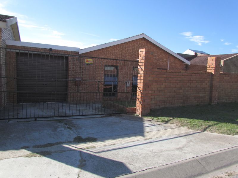 Front exterior view of a single-story face brick house featuring a metal garage door, gated driveway, and perimeter brick walling.